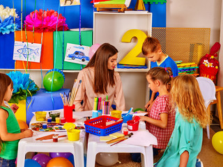 Children with teacher woman painting on paper at table in kindergarten . Children with teacher make...