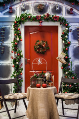 Fototapeta na wymiar Porch with red door with Christmas wreath and holiday decorations