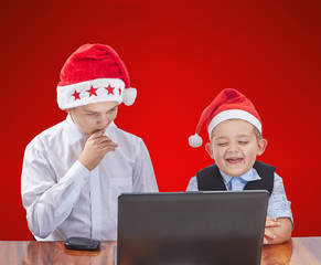 Children in caps Santa Claus looking at a laptop on a red background