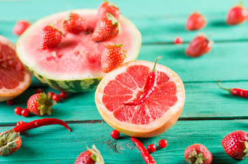 Fresh baby watermelon, strawberries, grapefruit halves, mini peppers, cranberries on wooden turquoise background. Colorful festive still life.