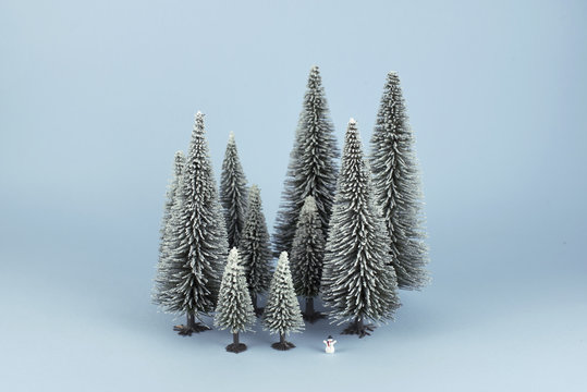 Bodegón mininalista de bosque en invierno con un diminuto muñeco de nieve. Fondo azul.
