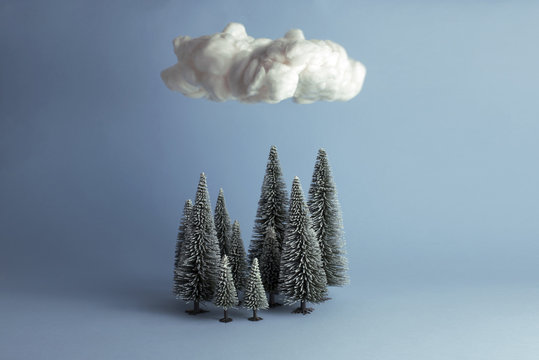 Bodegón mininalista de bosque en invierno sobre el que flota una nube. Fondo azul con sombras.