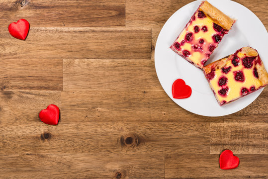 Raspberry cake on white plate and red hearts on wooden background. Valentines Day background
