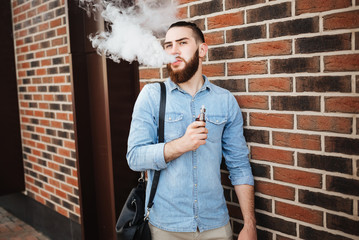Young man with beard vaping an electronic cigarette outdoor.  Casual hipster smoke vaporizer. Vaping