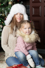 The mother and her child sit next to the Christmas tree. Portrait of a woman with a little girl. 