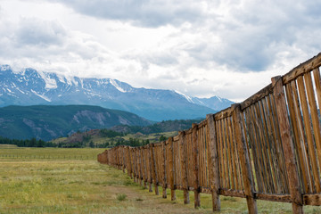 Long wooden fence in a field. In the distance the mountains.