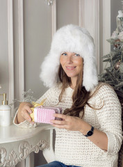 Beautiful girl is holding a gift. Portrait of a woman is near the Christmas tree. 