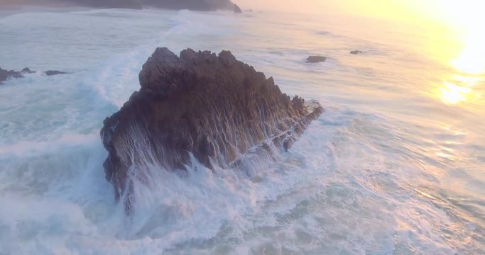 Amazing aerial shot of small waves hitting the beach and cliffs in Portugal. Flying over stormy sea, above the splashes of water, untouched, powerful nature.