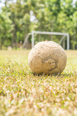 Old football on a grass field with white goal at the background.