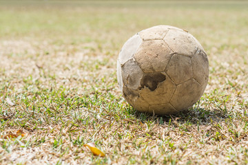 Old leather football on the dry yellow grass field.