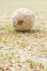 Old leather football on the dry yellow grass field.