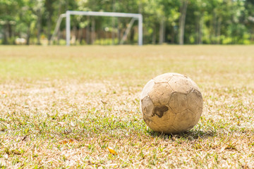 Old football on a grass field with a white goal at the backgroun
