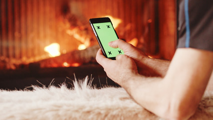 Unrecognizable Man Hands Using SmartPhone by the Burning Firepla