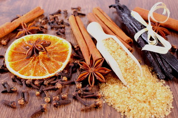 Brown sugar cane, fragrant vanilla pods and cinnamon sticks, star anise, cloves and dried orange on wooden board, seasoning for cooking or baking