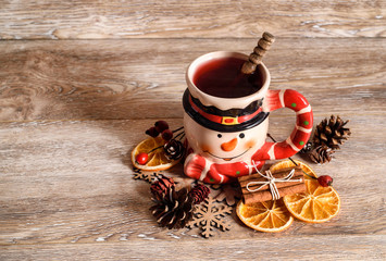 Christmas background with mulled wine in snowman mug, orange, cinnamon and pine cone on wood background