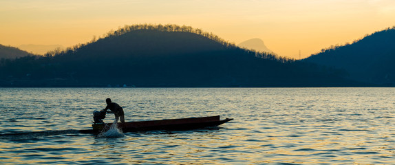 silhouette of a man are boating in the dam on the morning.