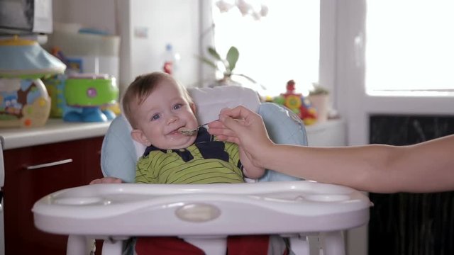 Mother feeding baby boy in home kitchen. Children and nutrition. HD.
