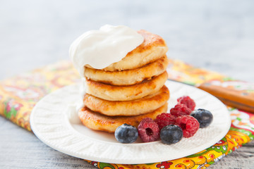 Summer cottage cheese pancakes on white plates on a  table with sour cream and berry, closeup, selective focus