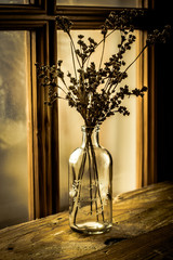 Dry wild field flowers in a vintage glass bottle on an aged wood table by a georgian window, selective focus