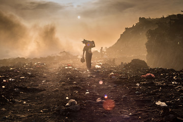 A waste picker is collecting reusable or recyclable materials in a open burning dump.