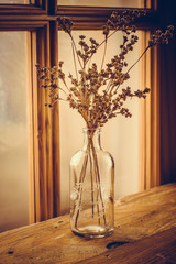 Bouqet of dry field flowers in a vintage glass vase on an aged wood table by a georgian window, toned