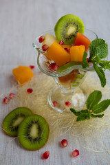Fruit desserts, salad of pineapple, papaya, pomegranate and mint, kiwi on light background