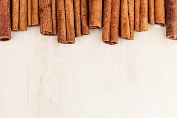 Cinnamon sticks closeup on white wood background. Christmas decorative border of cinnamon sticks spice. Top view.