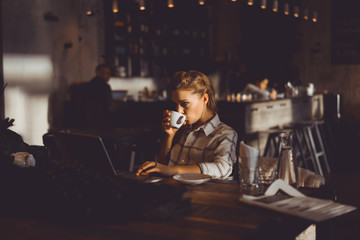 Fototapeta na wymiar outdoor portrait of a young girl she works as a freelancer in a cafe drinking a delicious hot Cup of coffee from text send mail loads the photo instagram freelancer drinking cappuccino in sunglasses