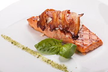 A piece of salmon steak with bacon and cheese.