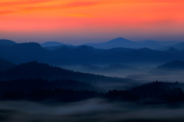 Cold misty foggy morning with twilight sunrise in a fall valley of Bohemian Switzerland park. Hills with fog, landscape of Czech Republic, National park Ceske Svycarsko. Beautiful foggy landscape.