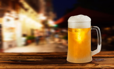 cold glass mug of beer with foam on the background of the street