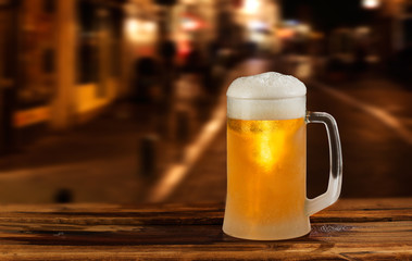 cold glass mug of beer with foam on the background of the street