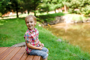 Smiling happy boy sitting on bench near lake. Summer time weeken