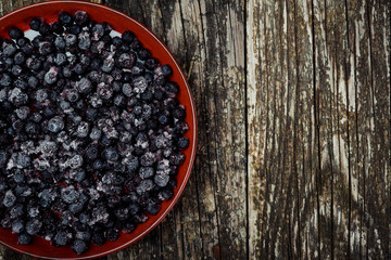 Frozen blueberries in a bowl on wooden background. Top view. Space for text.