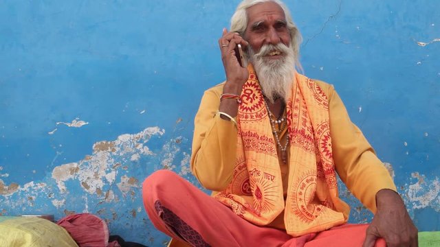 Wide shot of an Indian sage on his cell phone, moving in, in Pushkar, Rajasthan
