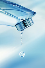 Water droplets drip flowing from chrome faucet in the sink in the kitchen or in the bathroom  close-up macro on a blue background. The concept of the idea of saving water and hygiene.