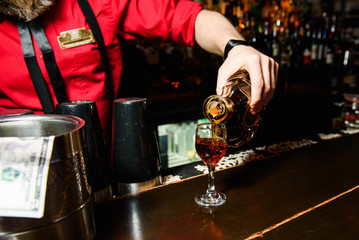 Waiter in red pours whisky in a glass