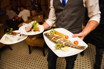 Waiter carries dishes with fish