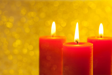 Drei brennende rote Kerzen vor Lichtern im Hintergrund