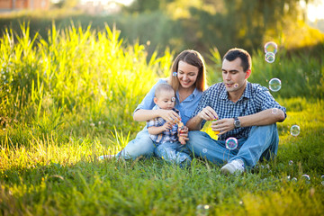 Naklejka na ściany i meble The family father, mother and son smiling and spend time together on the bright green grass.