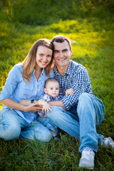 The family father, mother and son smiling and spend time together on the bright green grass.