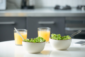 Two bowls of salad and glasses of orange juice on a white kitchen table. Healthy breakfast for couple. Light snack to promote a healthy day, vegetables as part of daily diet
