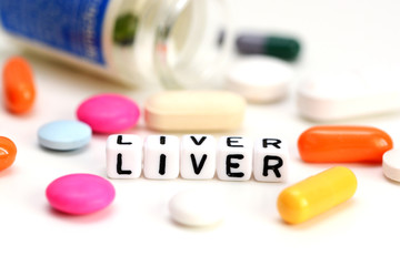 Liver problems concept with close-up of colorful medical pills and liver word on white background