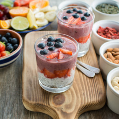 Healthy breakfast: coconut milk chia pudding topped with berry smoothie with blueberries and strawberries on top, served with various fruits and nuts, selective focus on the cut strawberries, square