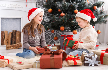 Fototapeta premium Happy children in santa hats unwrapping christmas presents