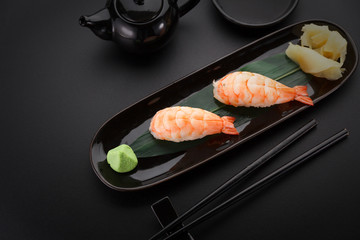 Shrimp sushi nigiri on a black plate over dark background