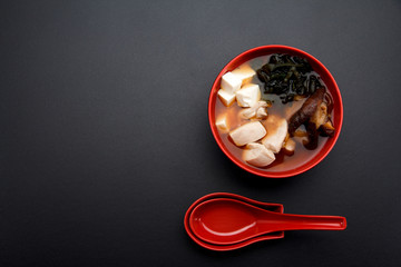 Japanese miso soup on a red bowl and spoon on the table.