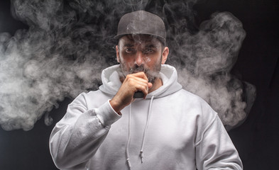 vaping man holding a mod. A cloud of vapor. Black background.