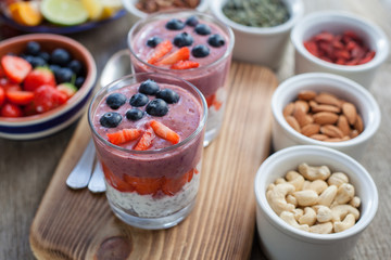 Healthy breakfast: coconut milk chia pudding topped with berry smoothie with blueberries and strawberries on top, served with various fruits and nuts, selective focus
