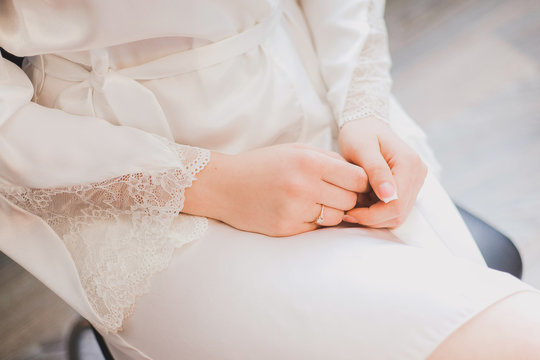 Morning of young beautiful woman sitting on chair with her hands crossed. Female fingernails with classic pink french manicure. Getting ready for wedding ceremony. Horizontal color image